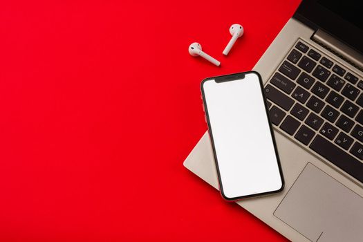 Tula, Russia - May 24,2019: Apple iPhone X and Airpods on red background with notebook. The screen of the smartphone is white. Mockup.