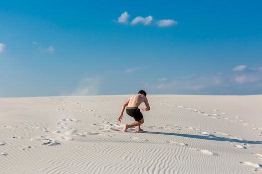 Young sporty man want doing acrobatic exercises on the sand near river. Portrait of young parkour man