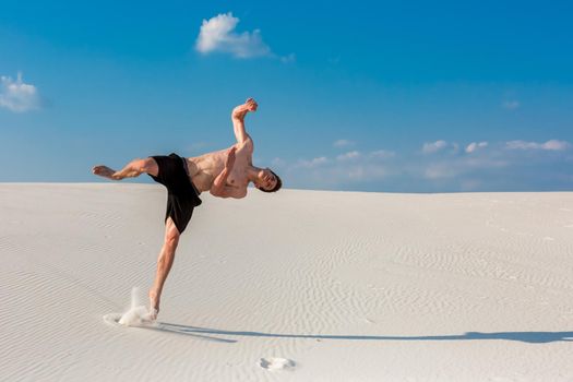 Portrait of young parkour man doing flip or somersault on the sand. Freezed moment of beginning doing bounce.