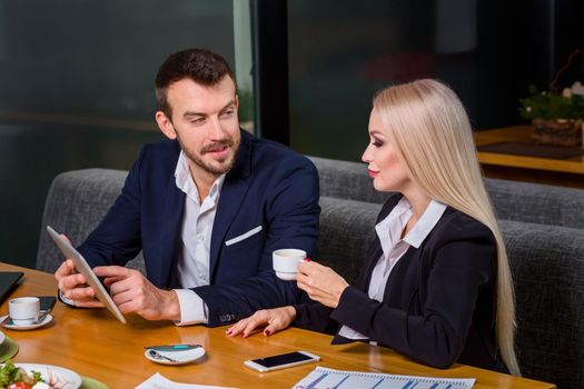 A woman and a man on a business lunch in a restaurant. exploring work on the tablet screen