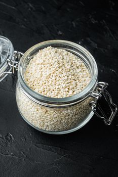 Decorticated sesame seeds set, in glass jar, on black stone background