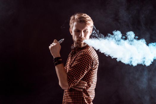 young man wearing a plaid shirt smokes an electronic cigarette on a black background