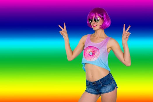 Portrait of young transgender woman in pink wig and sunglasses shows victory sign on rainbow background - image