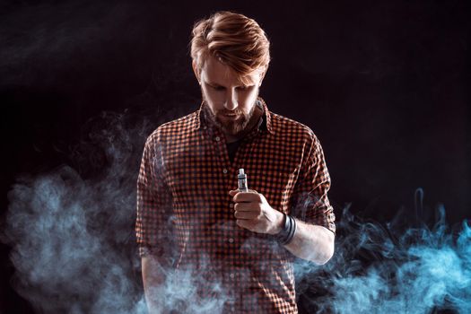 young man wearing a plaid shirt smokes an electronic cigarette on a black background