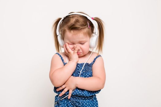 Cute little girl in headphones listening to music using a tablet on white background. The child does not look at the camera