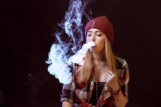 young woman smoking electronic cigarette on black background. Copy space