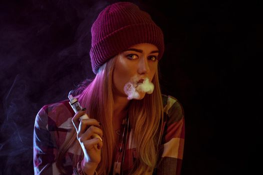 young woman smoking electronic cigarette on black background. woman looking at the camera