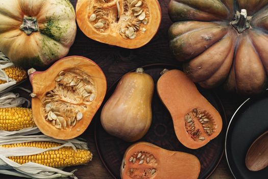 Corn cob and pumpkin on brown wooden board close up