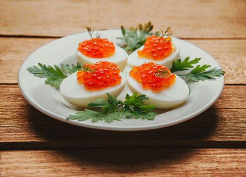 Appetizer boiled eggs half with red salmon caviar and parsley on plate on a wooden background