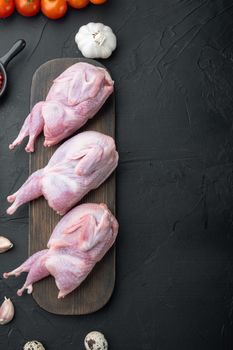 Whole quails meat with spices, herbs, vegetables, top view, on black textured background with copy space