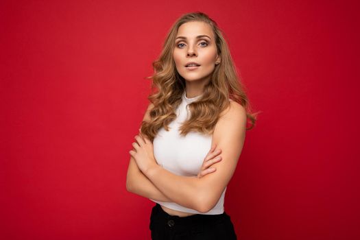 Portrait photo of young beautiful pretty self-confident assertive cool blonde woman with sincere emotions wearing stylish white top isolated over red background with free space.