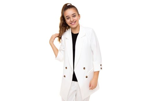 Photo of beautiful cute adorable positive smiling brunette teenage girl with ponytail in stylish white jacket and white pants isolated on white background with copy space for text.