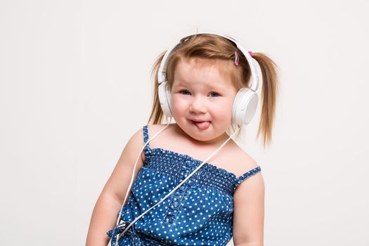 Cute little girl in headphones listening to music using a tablet and smiling on white background. A child looks at the camera
