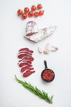 Sliced cuts of longaniza, dry cured spanish sausage with herbs and spices on white surface, flat lay.