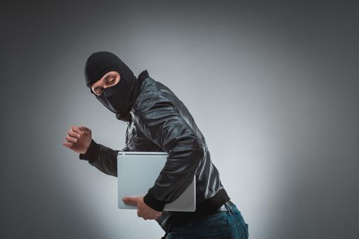 Thief stealing a laptop computer. Isolated on gray background. Studio shot