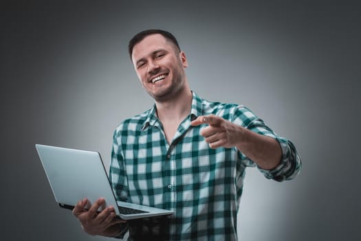 Attractive business man model in green shirt isolated on gray working with laptop, showing something by left hand. Caucasian guy.