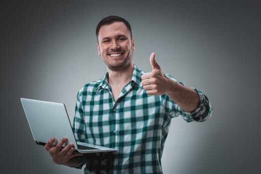 Attractive business man model in green shirt isolated on gray working with laptop, showing something by left hand. Caucasian guy.
