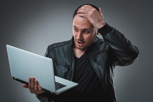 Portrait of young handsome man using laptop, wearing black leather jacket. Studio shot. Emotions