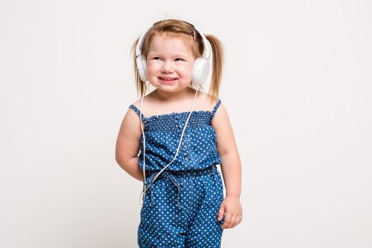 Cute little girl in headphones listening to music using a tablet and smiling on white background. The child does not look at the camera