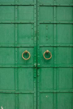 large antique wooden green doors with ring-shaped handles.