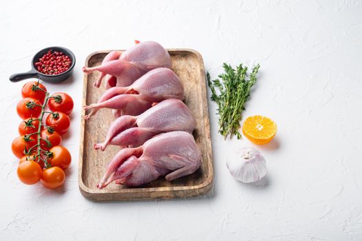 Whole quails meat with spices, herbs, vegetables, on white textured background with copy space