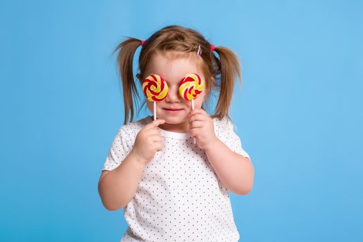 Beautiful little female child holding huge lollipop spiral candy smiling happy isolated on blue background. In children loving sweet and caramel concept