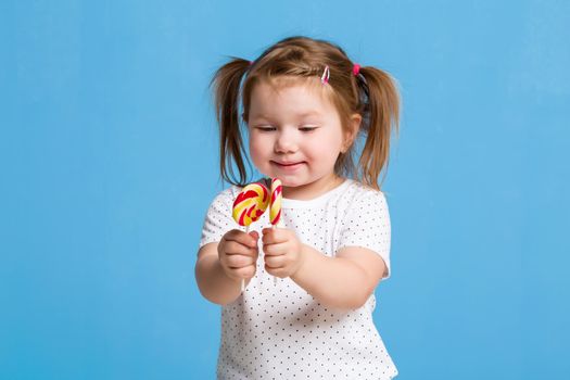 Beautiful little female child holding huge lollipop spiral candy smiling happy isolated on blue background. In children loving sweet and caramel concept