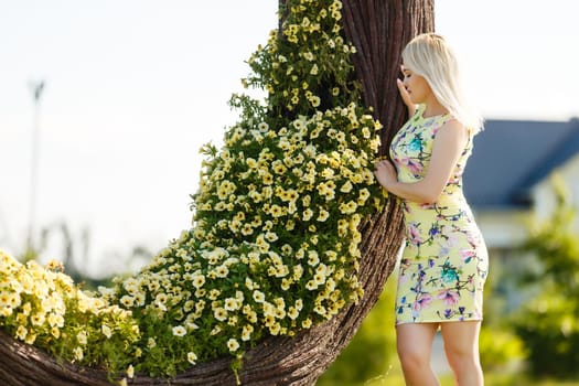 Beautiful young woman in nice dress posing on colorful wall of flowers. Fashion photo, nice hair, big smile