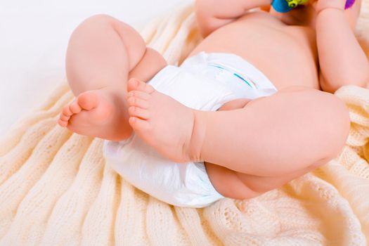 feet of a six months old baby wearing diapers lying in bed at home