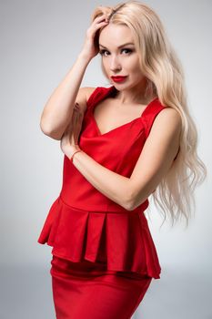 Glamorous young woman in red dress on gray background. She looks into the camera