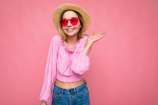 Photo shot of beautiful positive young blonde woman wearing summer casual clothes and stylish sunglasses isolated over colorful background looking to the side.