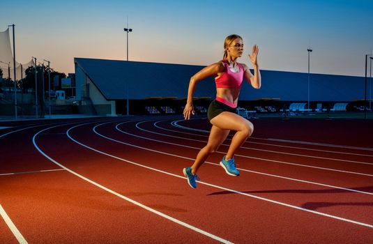 Runner sprinting towards success on run path running athletic track. Goal achievement concept. Female athlete sprinter doing a fast sprint for competition on red lane at an outdoor field stadium.