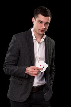 Young caucasian man in a dark suit and a white shirt holding two aces in his hand on black background. Gambling concept. Casino