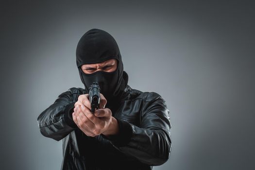 Burglar or terrorist in black mask shooting with gun. A man in the studio on a black-and-gray background