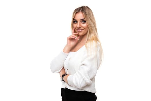 Photo of a charming beautiful pretty amazing positive young blonde woman with makeup in a stylish white knitted sweater and black pants isolated on a white background with copy space for text.