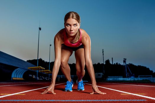 Portrait of beautiful woman ready to start running. Female athlete sprinter doing a fast sprint for competition on red lane at an outdoor field stadium.