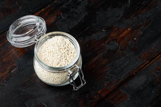 Decorticated sesame seeds set, in glass jar, on old dark wooden table background , with copyspace and space for text