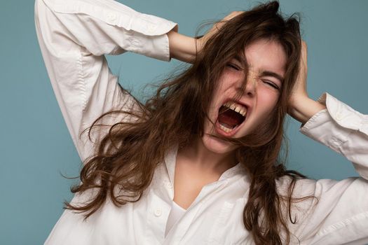 Attractive emotional cute nice adorable tender young curly brunette woman wearing white shirt isolated on blue background and shouting.