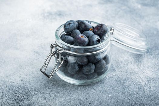 Ripe blueberry in glass jar, on textured background.