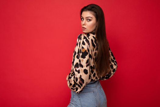 Image of a beautiful young brunette woman dressed in animal printed blouse posing isolated over red background with copy space.
