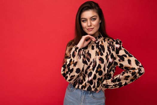 Image of a beautiful young brunette woman dressed in animal printed blouse posing isolated over red background with copy space.