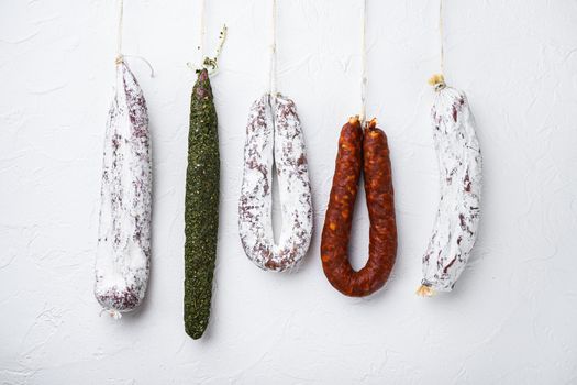 Traditional dry cured sausages meat hanging on white textured background.