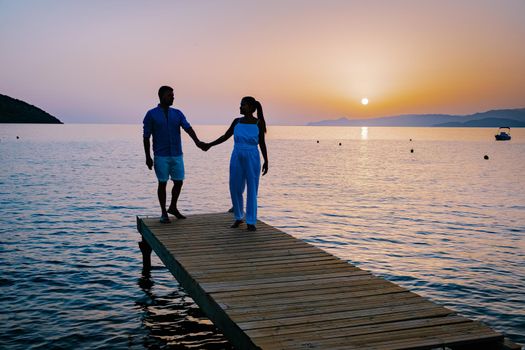 a couple seated on a wooden jetty, looking at colorful sunset on the sea, men, and women watching a sunset in Crete Greece Europe