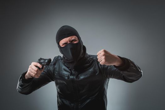 Masked robber with gun, looking into the camera. Studio shot on gray background. Emotions