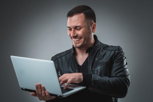 Man in black jacket looking at laptop, half turn. Holding opened laptop and working. Emotion. Indoors, studio, waist up, profile