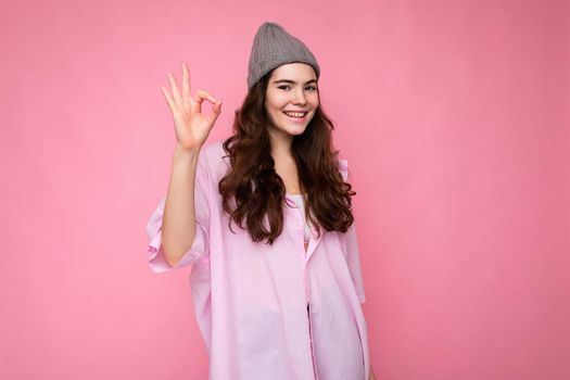 Photo of young positive happy smiling beautiful woman with sincere emotions wearing stylish clothes isolated over background with copy space and showing ok gesture. It's okay.