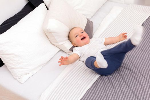 From above of pleased toddler in pajamas laughing while lying on modern bed at home