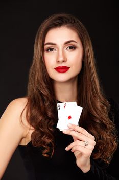 Sexy curly hair brunette in black dress posing with two aces cards in her hands, poker concept on black background. winning combination