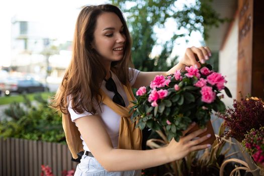 young beautiful brunette woman enjoying flowers in pots on the porch of a flower shop.