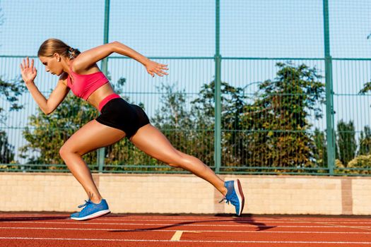 Runner sprinting towards success on run path running athletic track. Goal achievement concept. Female athlete sprinter doing a fast sprint for competition on red lane at an outdoor field stadium.